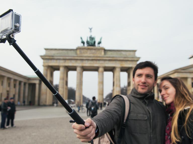 Zwei Touristen machen am Brandenburger Tor in Berlin ein Selbstporträt mit einem "Selfie-Stick"