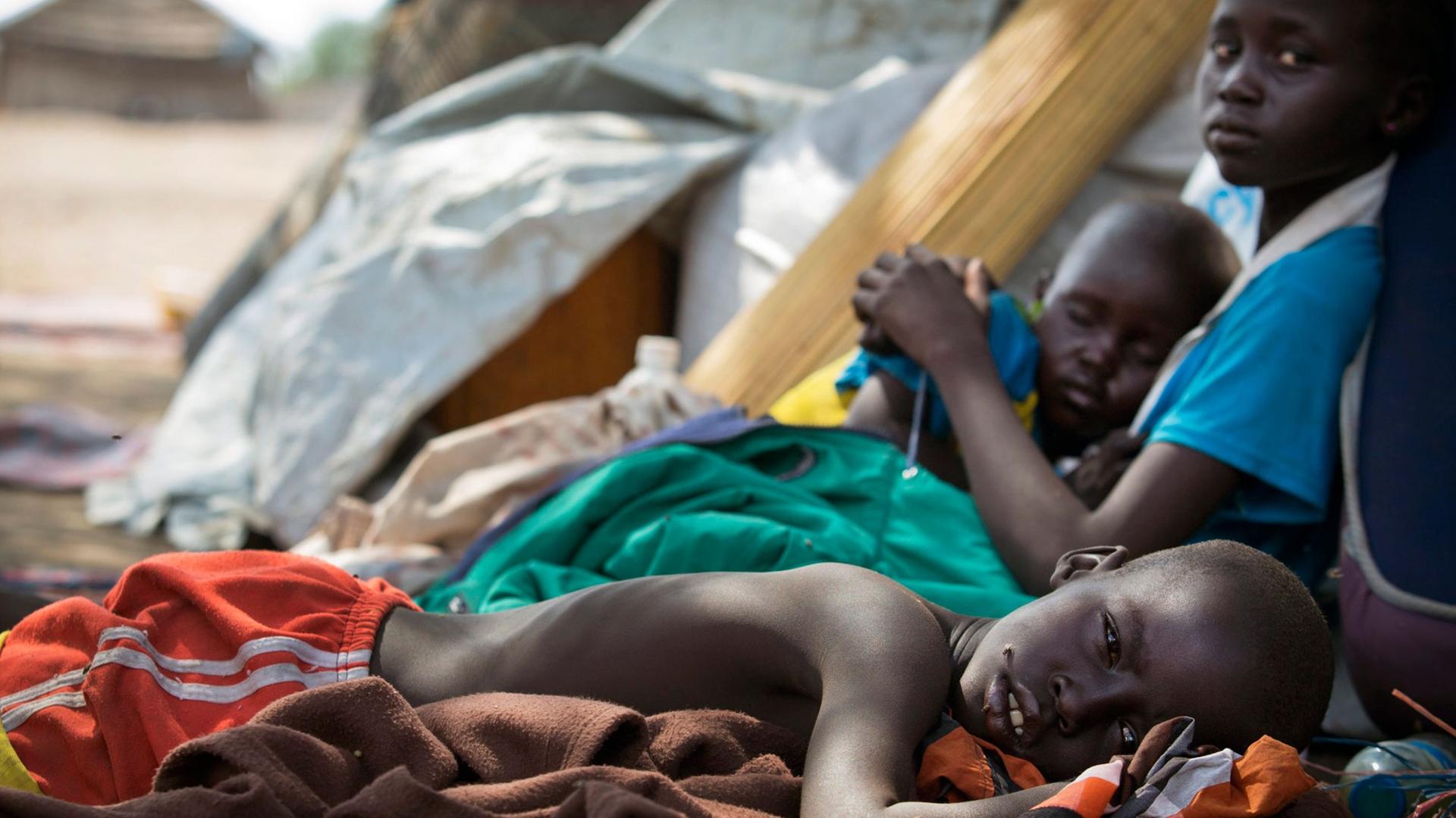 Ein Foto des Kinderhilfswerks UNICEF zeigt drei Kinder in der südsudanesischen Stadt Mingkaman, während sie erschöpft darauf warten, als Hilfesuchende registriert zu werden. Ein Foto des Kinderhilfswerks UNICEF zeigt drei Kinder in der südsudanesischen Stadt Mingkaman, während sie erschöpft darauf warten, als Hilfesuchende registriert zu werden.