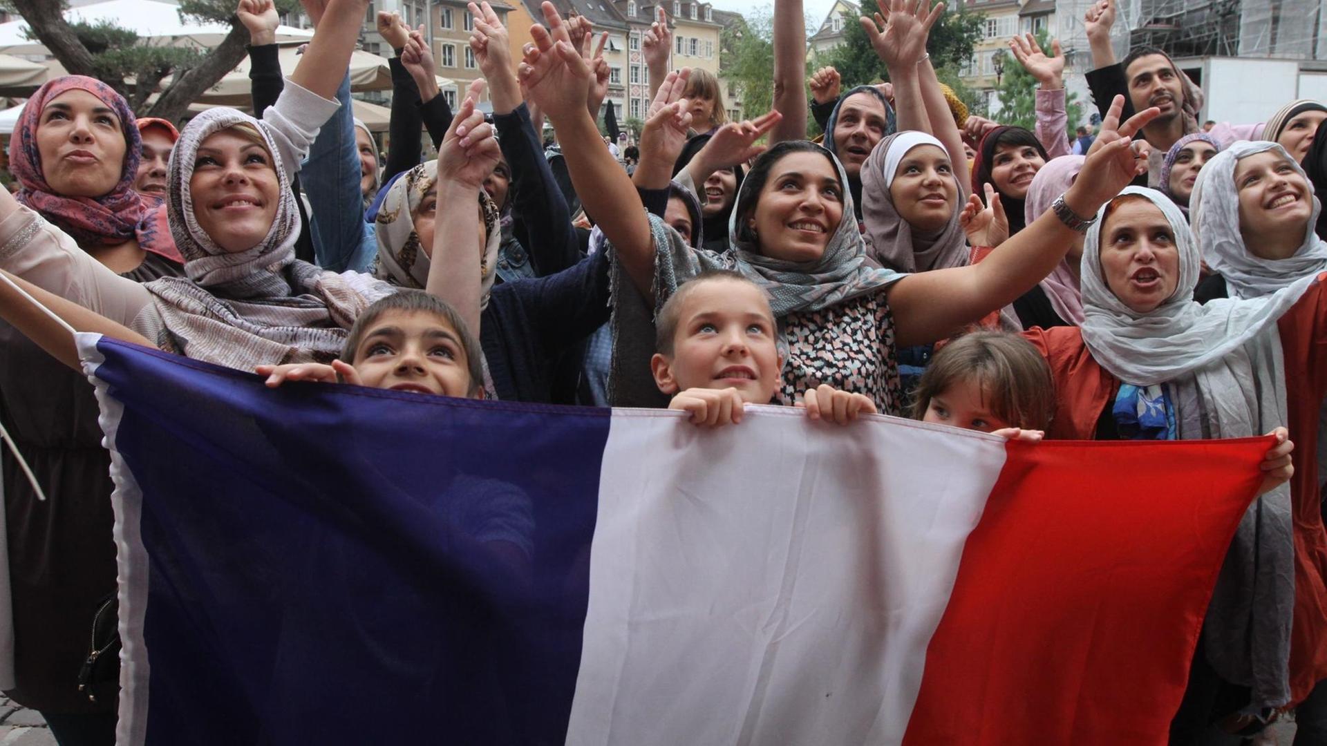 Foto einer Demonstration in Mulhouse gegen die Diskriminierung verschleierter Musliminnen - die Demonstranten halten eine große französische Flagge als Transparent in Händen. Foto: Darek Szuster / dpa Foto einer Demonstration in Mulhouse gegen die Diskriminierung verschleierter Musliminnen - die Demonstranten halten eine große französische Flagge als Transparent in Händen. Foto: Darek Szuster / dpa