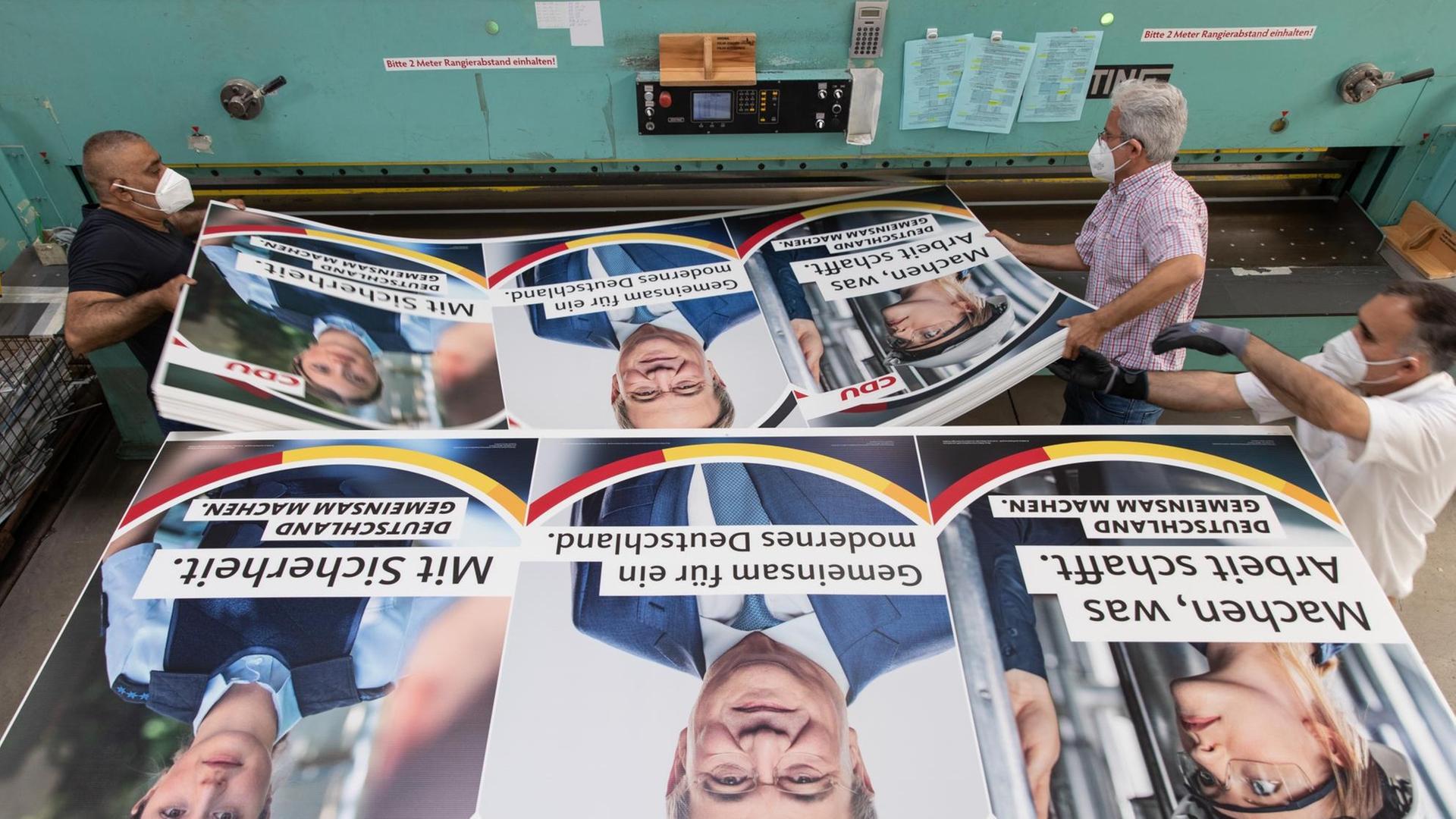 Druckereimitarbeiter legen Wahlplakate der CDU mit einem Bild des Parteivorsitzenden und Bundeskanzlerkandidaten Armin Laschet darauf in eine Zuschneidemaschine. Druckereimitarbeiter legen Wahlplakate der CDU mit einem Bild des Parteivorsitzenden und Bundeskanzlerkandidaten Armin Laschet darauf in eine Zuschneidemaschine.
