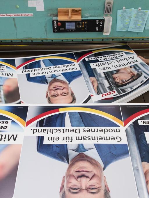Druckereimitarbeiter legen Wahlplakate der CDU mit einem Bild des Parteivorsitzenden und Bundeskanzlerkandidaten Armin Laschet darauf in eine Zuschneidemaschine.