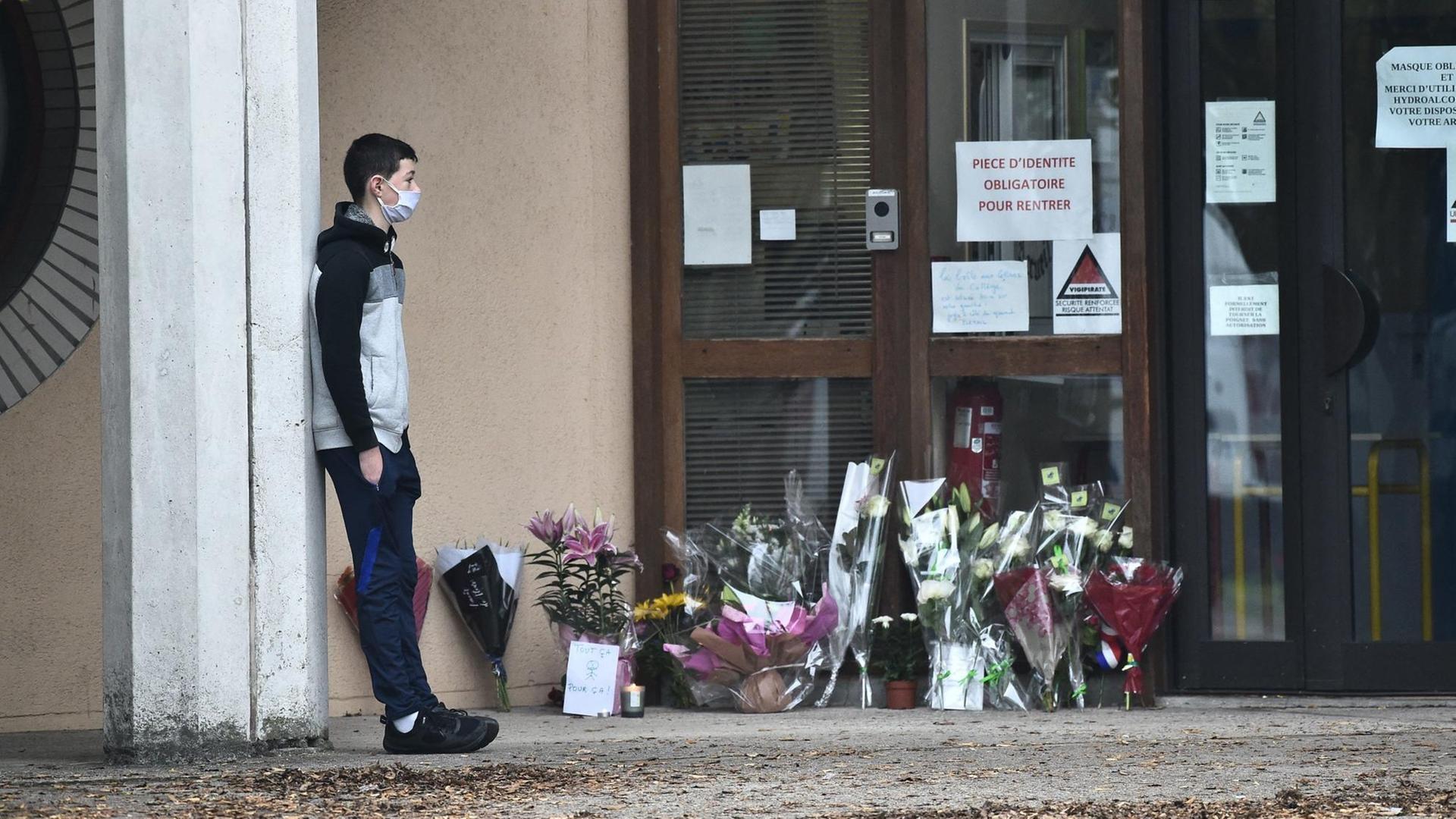 Ein Schüler trauert vor seiner Schule in Conflans-Sainte-Honorine. vIele Menschen haben an deren Eingang Blumen niedergelegt, um an dern ermordeten Lehrer zu erinnern.