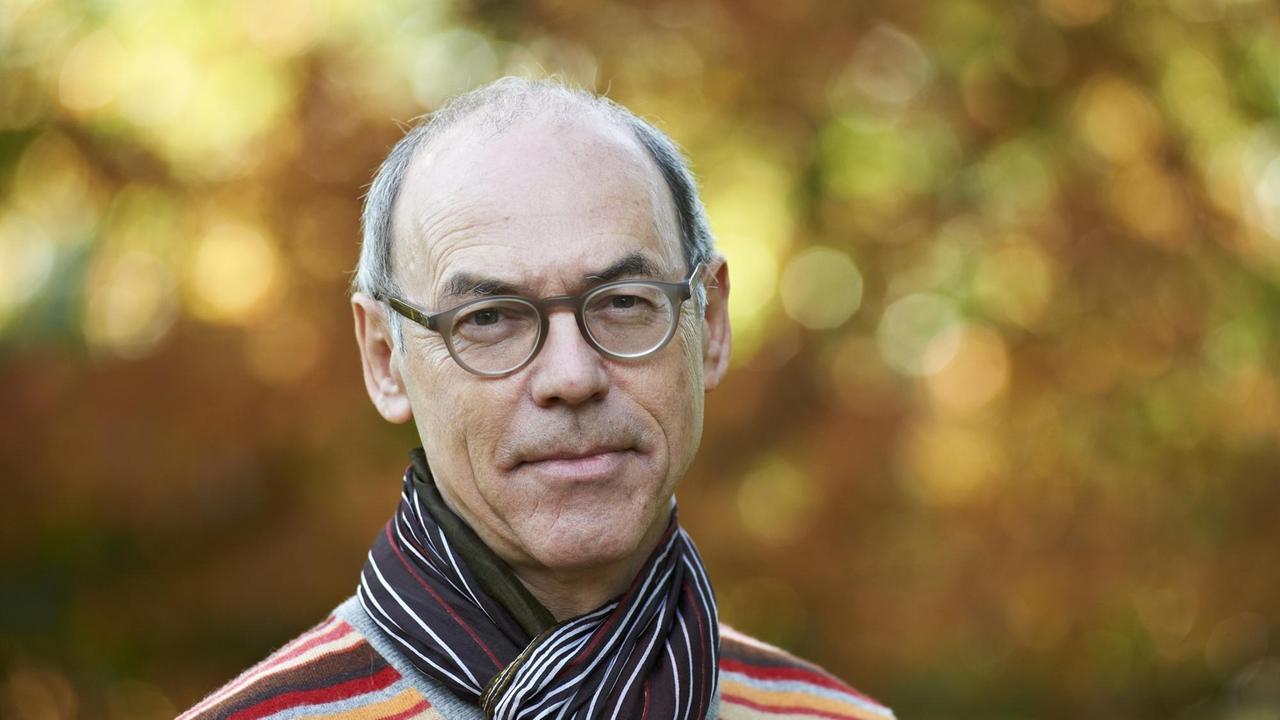 Porträt des Kulturphilosophen Josef Früchtl, lächelnd vor Herbstlaub, er trägt einen in Rottönen gestreiften Pullover und ein dunkles, gestreiftes Halstuch. Porträt des Kulturphilosophen Josef Früchtl, lächelnd vor Herbstlaub, er trägt einen in Rottönen gestreiften Pullover und ein dunkles, gestreiftes Halstuch.