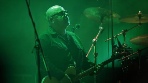 Pixies-Frontmann Charles Thompson alias Black Francis steht auf einer grün ausgeleuchteten Bühne, die Gitarre hat er umgehängt.
