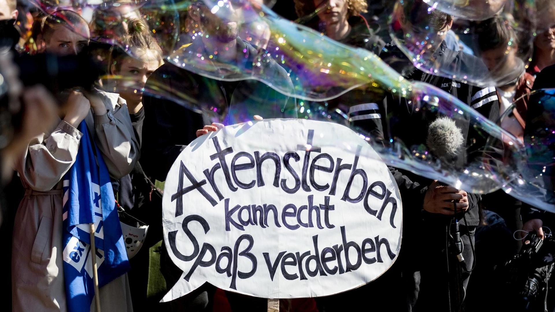 "Artensterben kann echt Spaß verderben" steht bei einer Kundgebung der Bewegung Extinction Rebellion an der Jannowitzbrücke auf dem Plakat eines Teilnehmers, während Seifenblasen vorbeiziehen