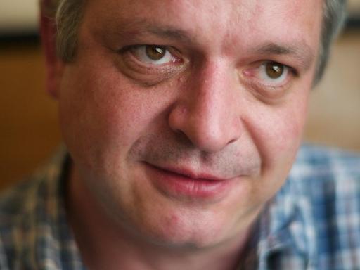 Der Stuttgarter Schriftsteller Ulf Stolterfoht sitz in einem Wiener Café, er trägt ein kariertes Hemd und blickt leicht an der Kamera vorbei.
