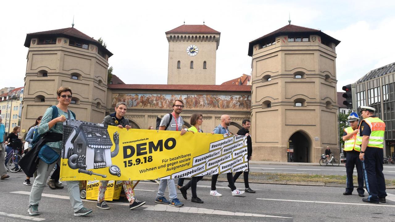 Teilnehmer einer Demonstration für bezahlbaren Wohnraum und gegen soziale Ausgrenzung gehen unter dem Motto #ausspekuliert auf die Straße. Sie halten ein gelb-schwarzes Banner mit der Aufschrift Demo 15.9.18, den Tag der Demonstration.