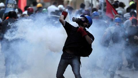 Mit einer Atemschutzmaske steht ein junger Mann in einer Tränengaswolke auf einem Platz in Istanbul