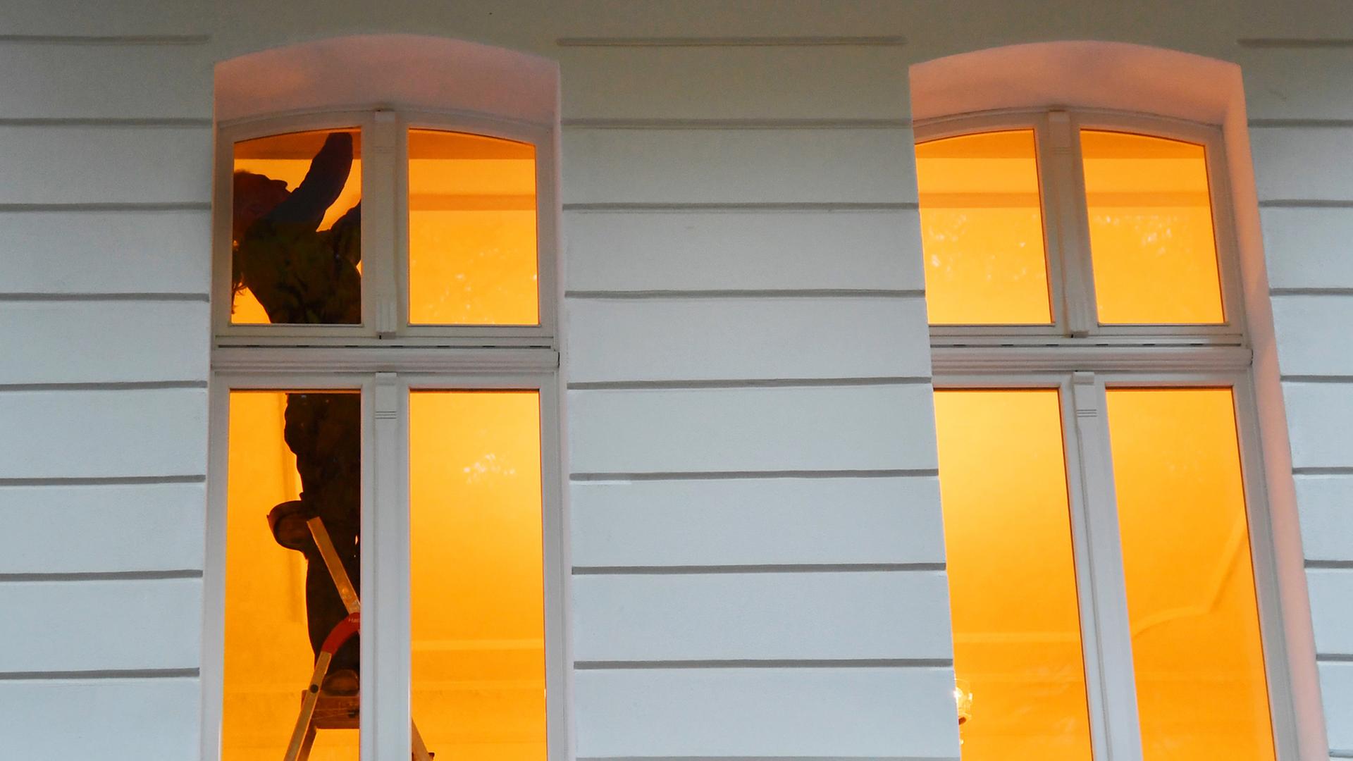 Ein Mann steht in Berlin an einem Fenster in einer Wohnung auf einer Leiter. Ein Mann steht in Berlin an einem Fenster in einer Wohnung auf einer Leiter.
