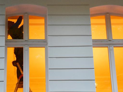 Ein Mann steht in Berlin an einem Fenster in einer Wohnung auf einer Leiter.