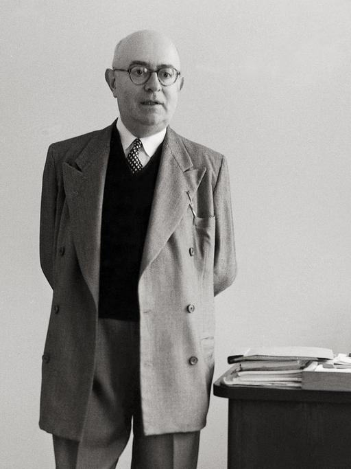 Die Aufnahme von 1958 zeigt den Philosophen Theodor W. Adorno mit hinter dem Rücken verschränkten Händen neben seinem Schreibtisch stehend.