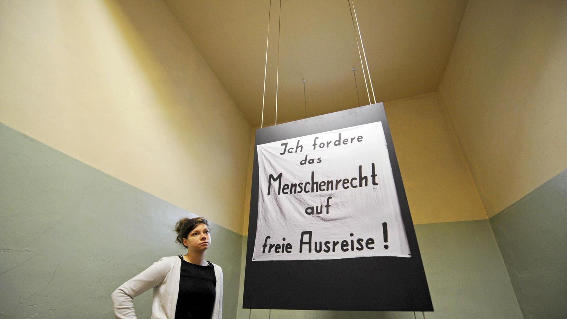 Eine Museumspädagogin steht in einer früheren Zelle des ehemaligen Stasigefängnis Andreasstraße in Erfurt, von der Decke hängt ein Plakat mit der Aufschrift "Ich fordere das Menschenrecht auf freie Ausreise!". Eine Museumspädagogin steht in einer früheren Zelle des ehemaligen Stasigefängnis Andreasstraße in Erfurt, von der Decke hängt ein Plakat mit der Aufschrift "Ich fordere das Menschenrecht auf freie Ausreise!".