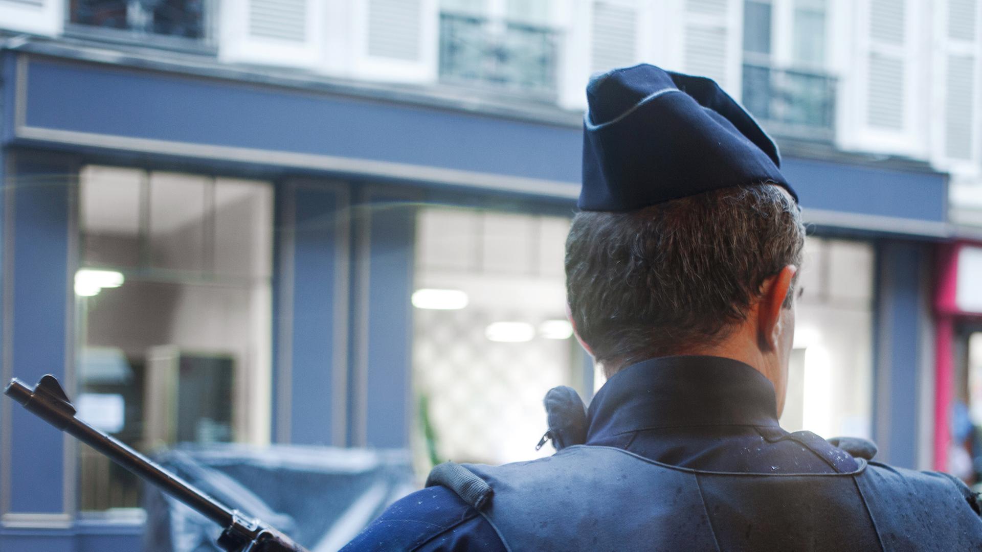 Ein bewaffneter Polizist steht in Paris vor einer Häuserzeile. Ein bewaffneter Polizist steht in Paris vor einer Häuserzeile.