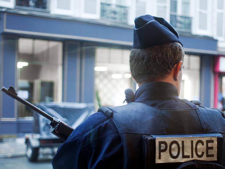 Ein bewaffneter Polizist steht in Paris vor einer Häuserzeile.