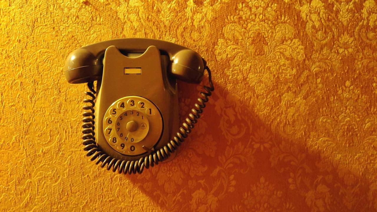 Ein altes Telefon mit Wahlscheibe vor einer Vintage-Tapete. Ein altes Telefon mit Wahlscheibe vor einer Vintage-Tapete.