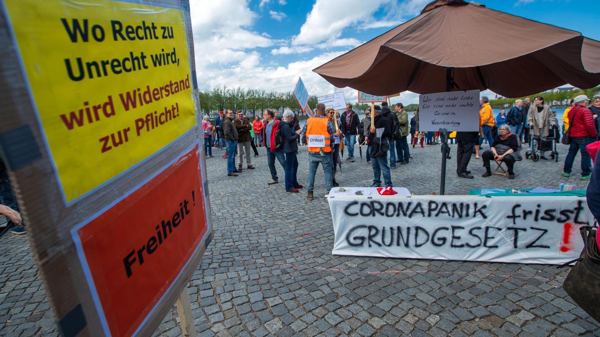 01.05.2020, Mecklenburg-Vorpommern, Schwerin: Ein Schild mit der Aufschrift «Wo Recht zu Unrecht wird, wird Widerstand zur Pflicht. Freiheit." (l) und ein Banner "Coronapanik frisst Grundgesetz" (r) sind bei der Mahnwache zu sehen, zu der sich am Pfaffenteich mehrere hundert Bürger versammeln und gegen die Corona-Schutzmaßnahmen protestieren. Nach Aufforderungen der Polizei wurde das Treffen aufgelöst. Foto: Jens Büttner/dpa-Zentralbild/dpa | Verwendung weltweit 01.05.2020, Mecklenburg-Vorpommern, Schwerin: Ein Schild mit der Aufschrift «Wo Recht zu Unrecht wird, wird Widerstand zur Pflicht. Freiheit." (l) und ein Banner "Coronapanik frisst Grundgesetz" (r) sind bei der Mahnwache zu sehen, zu der sich am Pfaffenteich mehrere hundert Bürger versammeln und gegen die Corona-Schutzmaßnahmen protestieren. Nach Aufforderungen der Polizei wurde das Treffen aufgelöst. Foto: Jens Büttner/dpa-Zentralbild/dpa | Verwendung weltweit