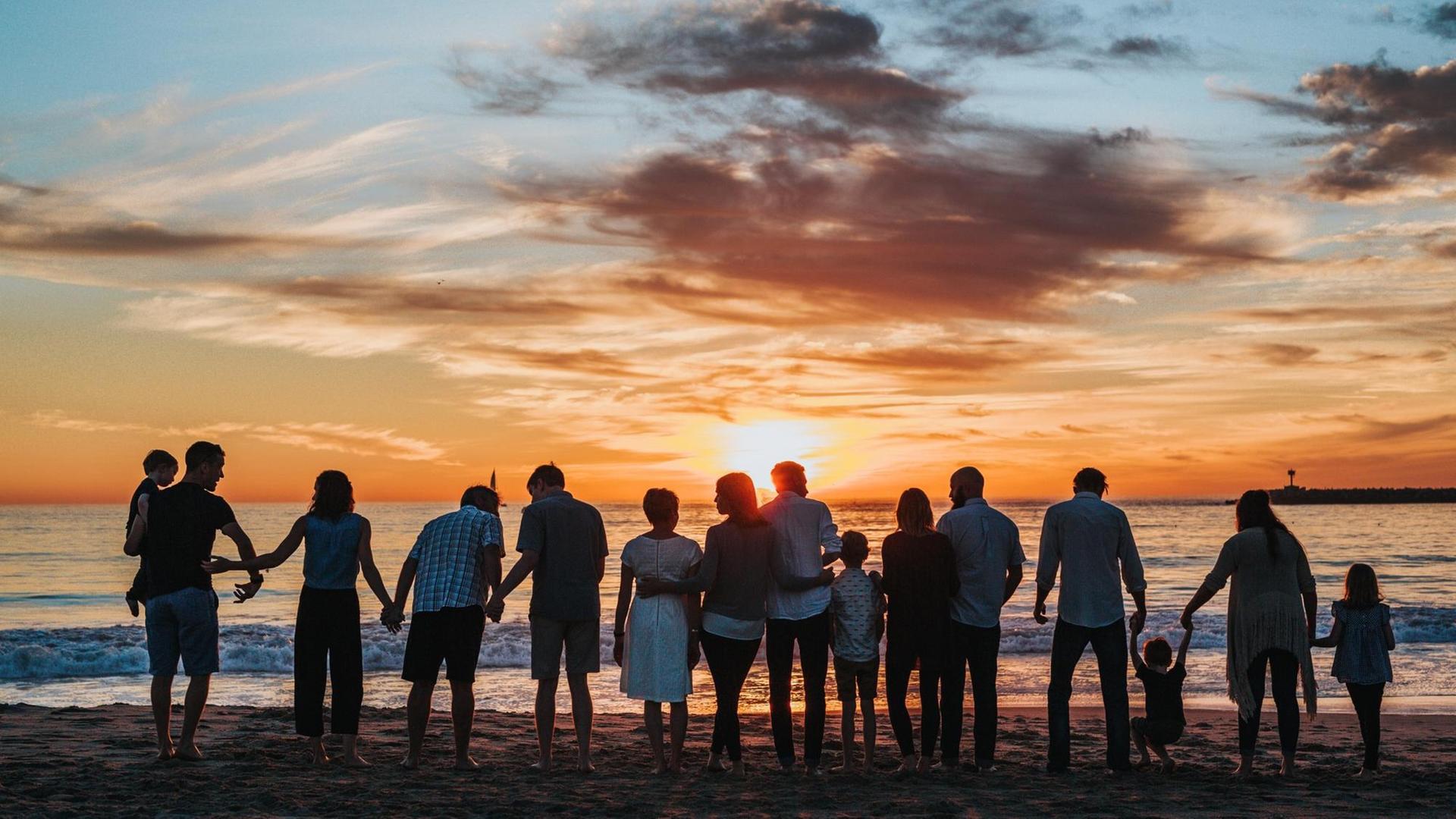 Eine Großfamilie mit mehreren Kindern steht am Strand mit den Rücken zur Kamera und betrachtet den Sonnenuntergang. Eine Großfamilie mit mehreren Kindern steht am Strand mit den Rücken zur Kamera und betrachtet den Sonnenuntergang.