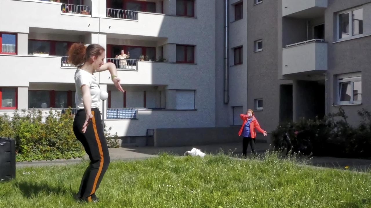 Zwei Frauen machen vor einem Haus Sportübungen. Auf dem Balkon dahinter macht eine weitere Frau auch mit. Zwei Frauen machen vor einem Haus Sportübungen. Auf dem Balkon dahinter macht eine weitere Frau auch mit.
