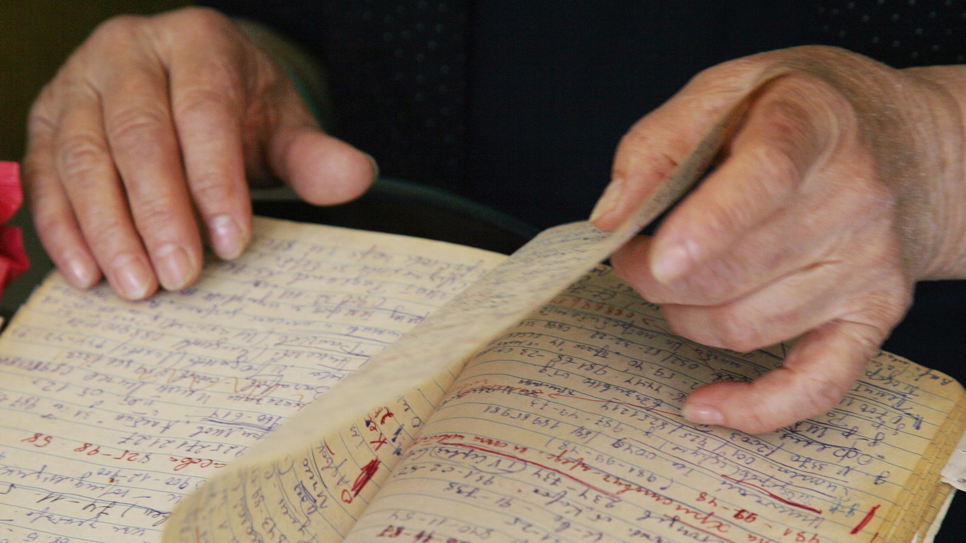 Eine ältere Frau blättert in einem Notizbuch - ihre Hände sind zu sehen. Eine ältere Frau blättert in einem Notizbuch - ihre Hände sind zu sehen.