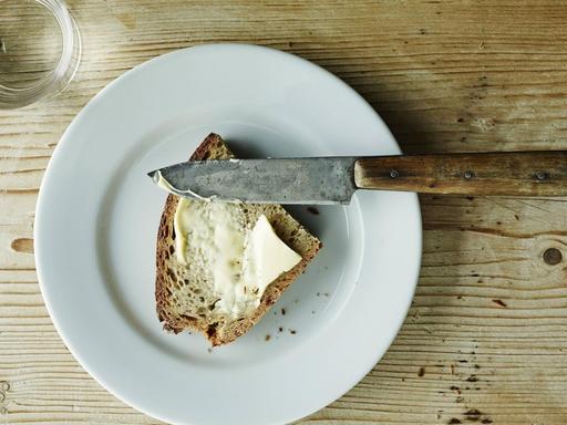 Auf einem Tisch stehen ein Wasserglas und eine Scheibe Brot mit Butter.