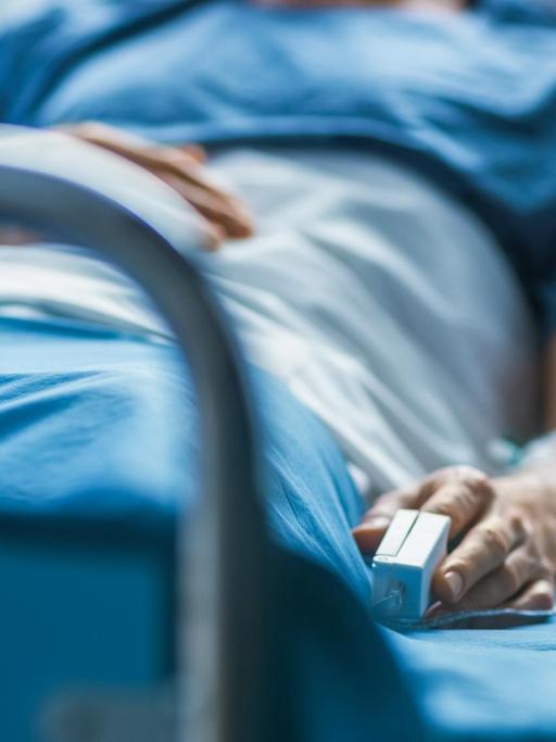 Eine Person liegt im Krankenhausbett und hat ein Gerät zur Überwachung des Herzzrhytmuses an seinem Finger.