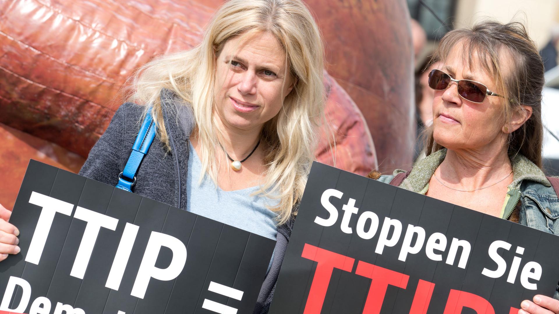 Zwei Frauen protestieren am 06.05.2014 vor dem Brandenburger Tor in Berlin gegen das Freihandelsabkommen TTIP zwischen der EU und den USA mit Transparenten. Zwei Frauen protestieren am 06.05.2014 vor dem Brandenburger Tor in Berlin gegen das Freihandelsabkommen TTIP zwischen der EU und den USA mit Transparenten.