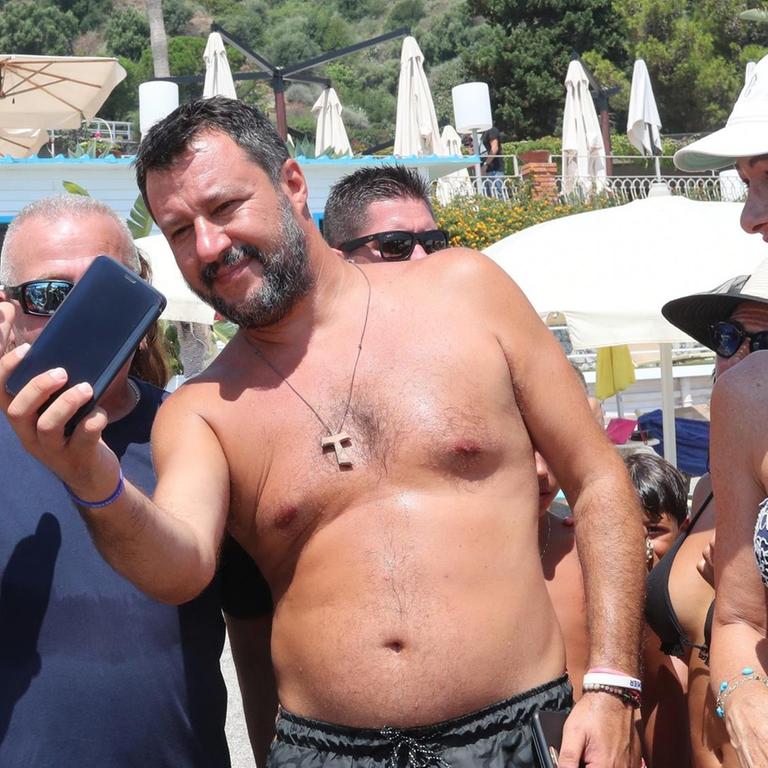 Das Foto zeigt Italiens Innenminister Matteo Salvini, der am Strand zusammen mit einem Mann ein Selfie macht.