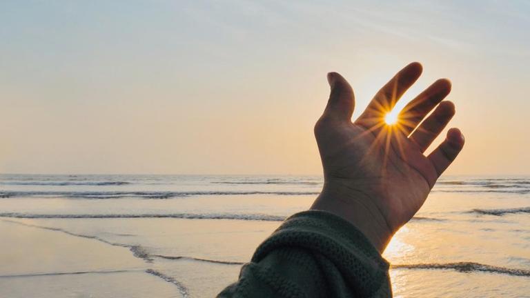 Eine Hand vor der untergehenden Sonne am Meereshorizont Eine Hand vor der untergehenden Sonne am Meereshorizont