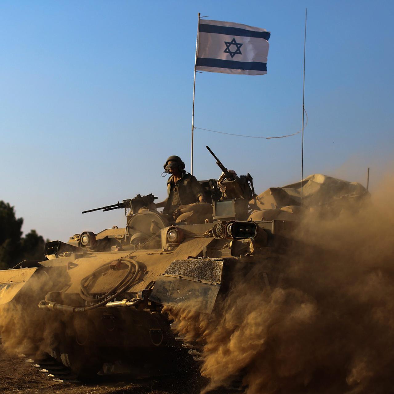 Israelische Soldaten mit Maschinengewehren fahren in einem Panzer, der reichlich Staub aufwirbelt, auf ihm steckt eine israelische Flagge