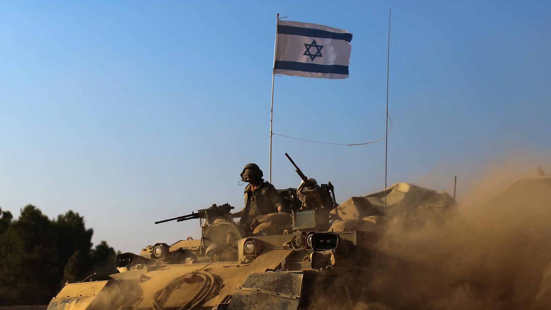 Israelische Soldaten mit Maschinengewehren fahren in einem Panzer, der reichlich Staub aufwirbelt, auf ihm steckt eine israelische Flagge Israelische Soldaten mit Maschinengewehren fahren in einem Panzer, der reichlich Staub aufwirbelt, auf ihm steckt eine israelische Flagge