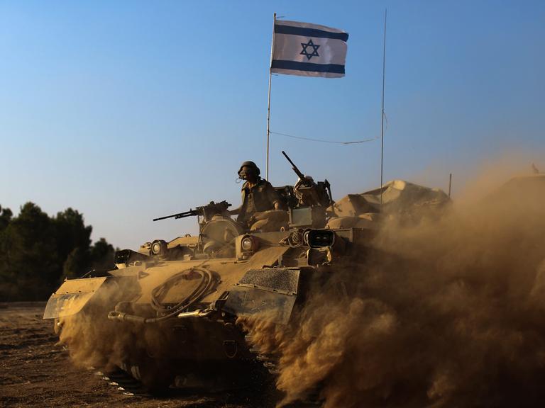 Israelische Soldaten mit Maschinengewehren fahren in einem Panzer, der reichlich Staub aufwirbelt, auf ihm steckt eine israelische Flagge