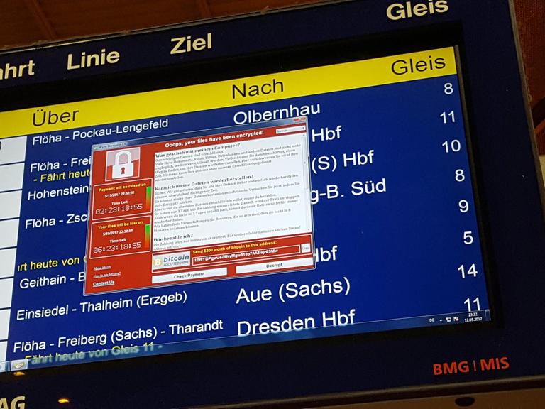 Die Anzeigetafel zeigt Zugabfahrten an, davor erscheint in rot der Text der Erpresser.
