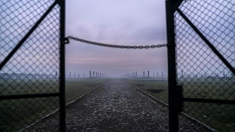 Sonnenaufgang im Morgennebel vor den halb offenen Drahttoren des Vernichtungslagers Auschwitz-Birkenau in Oswiecim, Polen.