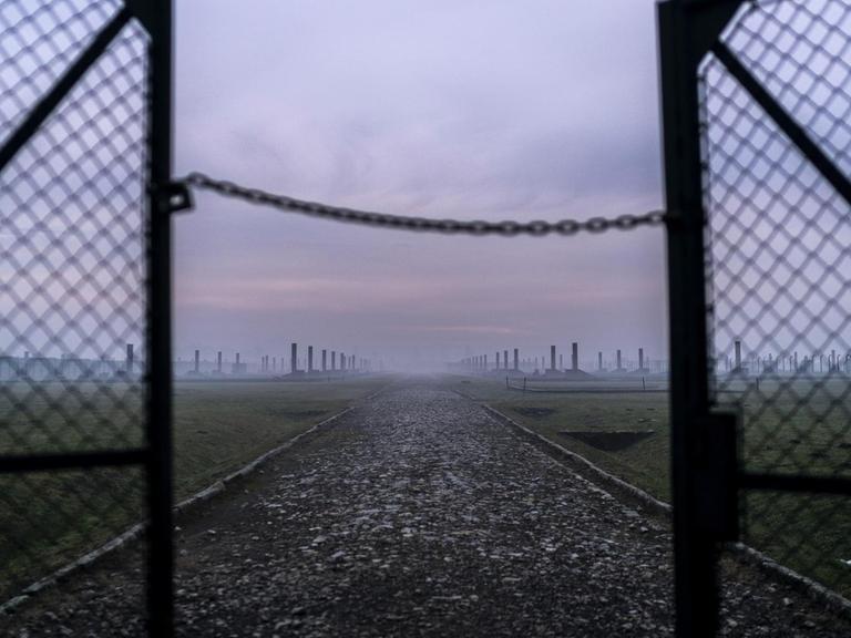 Sonnenaufgang im Morgennebel vor den halb offenen Drahttoren des Vernichtungslagers Auschwitz-Birkenau in Oswiecim, Polen.