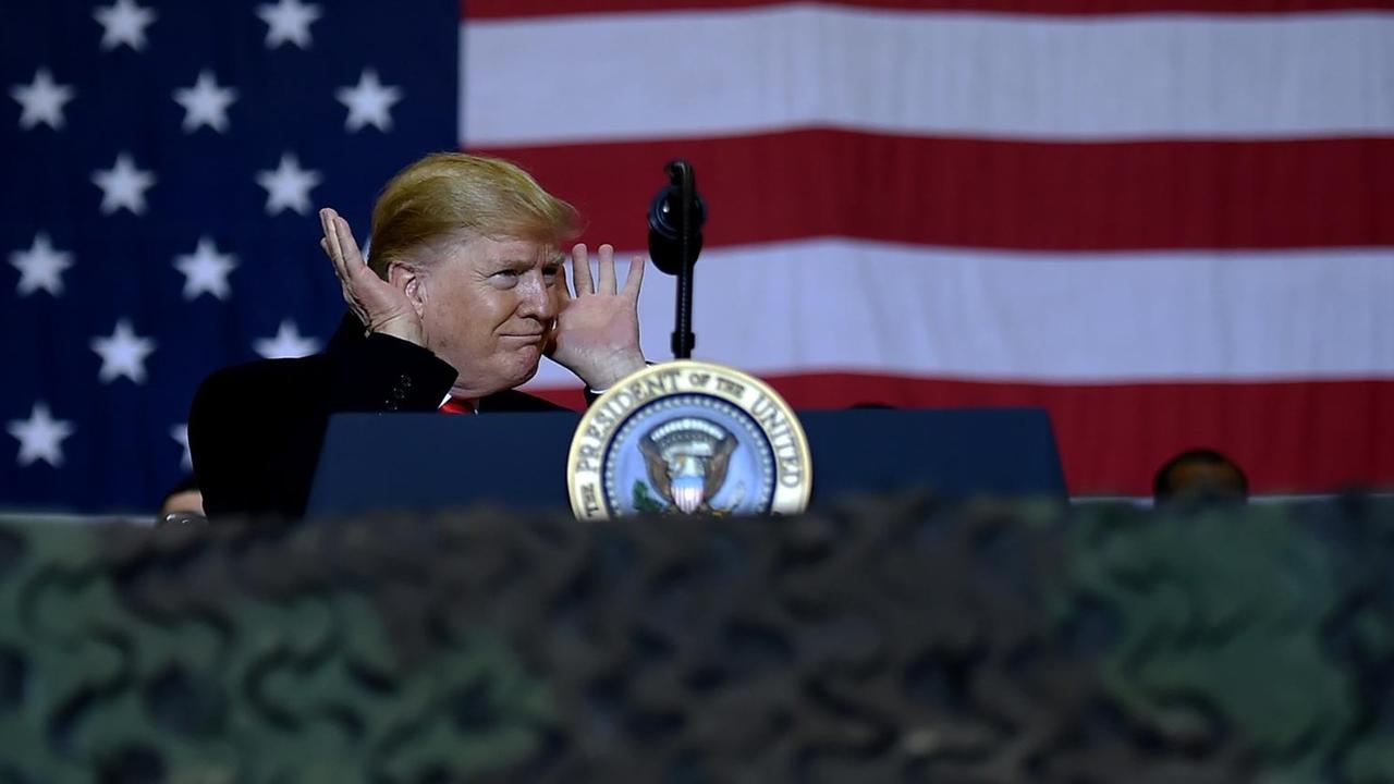 US-Präsident Donald Trump auf Kurzbesuch bei den US-Soldaten in Afghanistan. Er steht an einem Redepult und hält sich die Hände an die Ohren, als warte er auf eine Reaktion des Publikums. US-Präsident Donald Trump auf Kurzbesuch bei den US-Soldaten in Afghanistan. Er steht an einem Redepult und hält sich die Hände an die Ohren, als warte er auf eine Reaktion des Publikums.