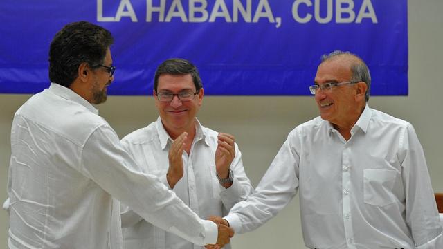 Die beiden weißgekleideten Männer schütteln sich lächelnd die Hand. Dazwischen steht der kubanische Außenminister Bruno Rodriguez, der ebenfalls lächelnd applaudiert. Auch er trägt ein weißes Hemd.