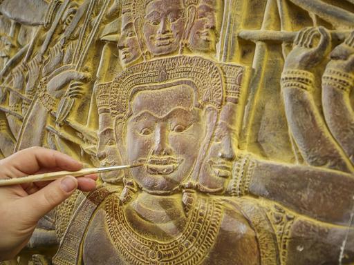 Eine Restauratorin arbeitet mit einem Pinsel an den Angkor Vat Reliefs.