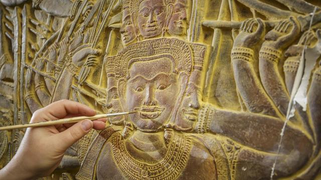 Eine Restauratorin arbeitet mit einem Pinsel an den Angkor Vat Reliefs.