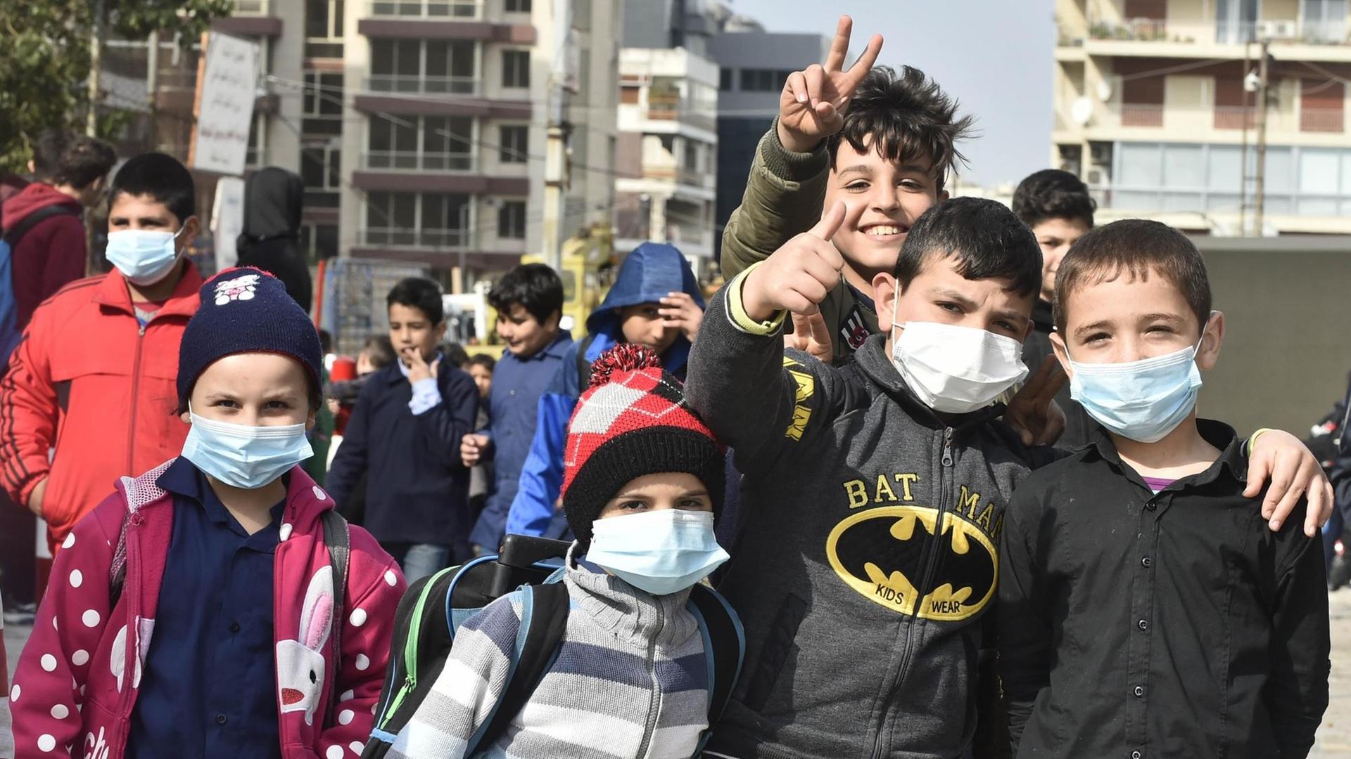 Eine Gruppe von jungen Schülern schaut in die Kamera, einige tragen Atemschutzmasken. Ein Junge im Hintergrund zeigt das Victory-Zeichen. Eine Gruppe von jungen Schülern schaut in die Kamera, einige tragen Atemschutzmasken. Ein Junge im Hintergrund zeigt das Victory-Zeichen.
