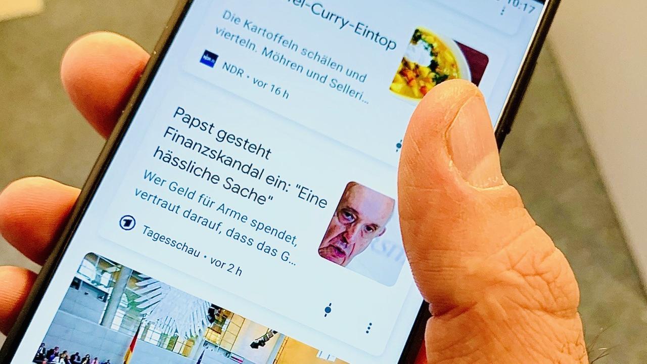 Nachrichtenmeldungen neben Rezepten - eine Hand hält ein Smartphone, auf dem Google "Discover" zu sehen ist Nachrichtenmeldungen neben Rezepten - eine Hand hält ein Smartphone, auf dem Google "Discover" zu sehen ist