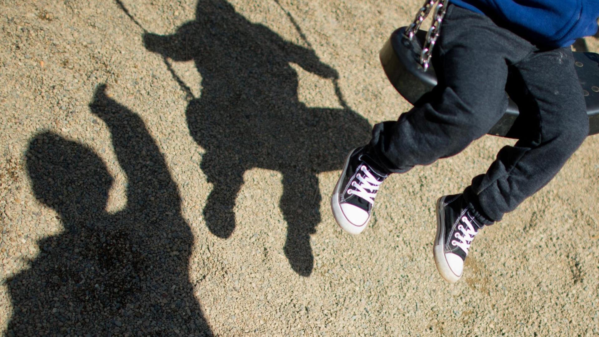 Ein Kind auf der Schaukel und der Schatten eines Mannes Ein Kind auf der Schaukel und der Schatten eines Mannes