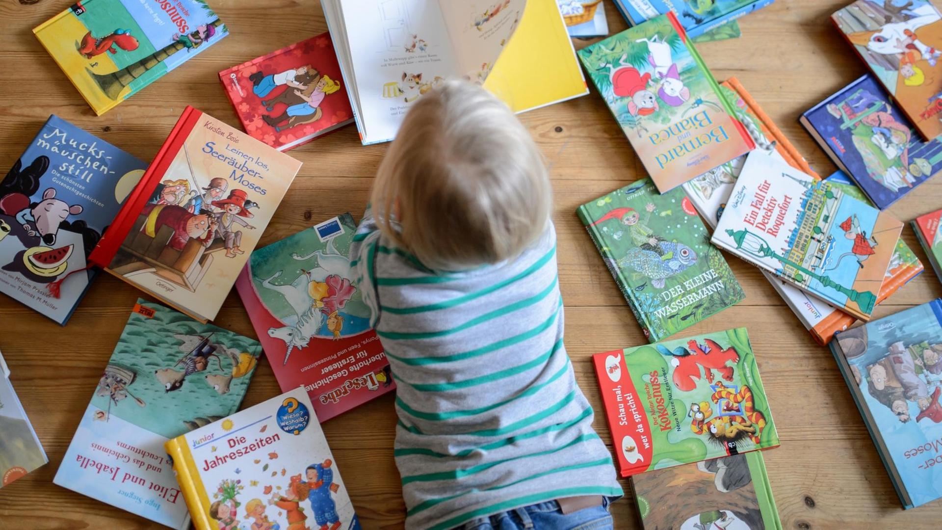 Ein Kind liegt zwischen vielen Büchern und schaut sich ein Buch an. Ein Kind liegt zwischen vielen Büchern und schaut sich ein Buch an.