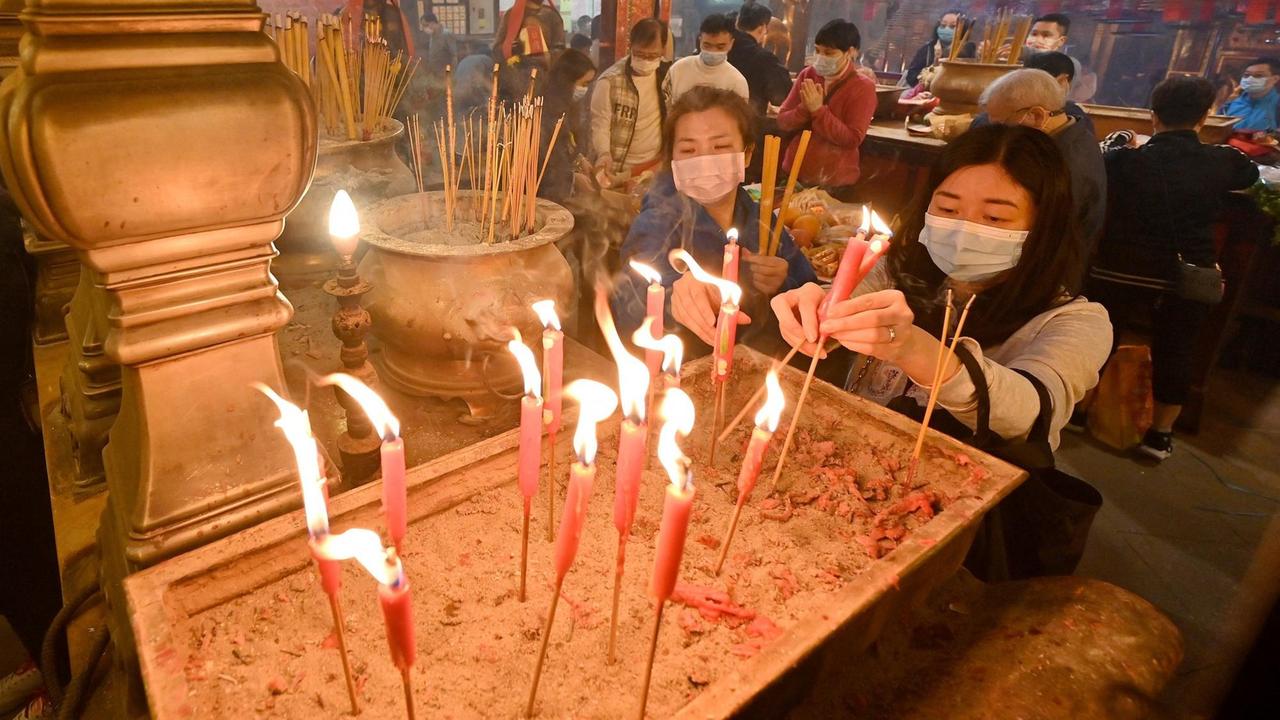 Frauen mit Mundschutz zünden in einem Tempel Räucherstäbchen und Kerzen an Frauen mit Mundschutz zünden in einem Tempel Räucherstäbchen und Kerzen an