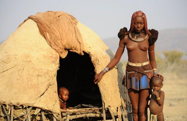 Eine Himba-Frau mit ihren zwei Kindern vor der Wohnhütte in Opuwo, Namibia