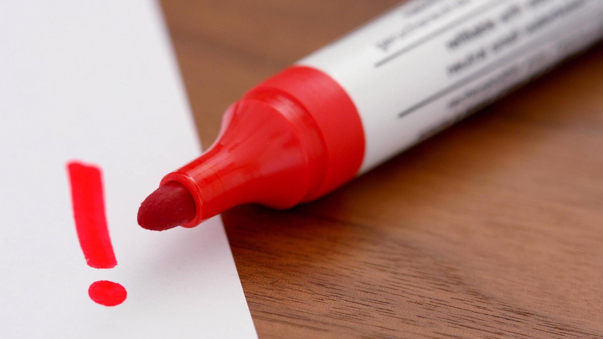 Ein roter Filzstift malt ein Ausrufezeichen auf ein Blatt Papier. Ein roter Filzstift malt ein Ausrufezeichen auf ein Blatt Papier.