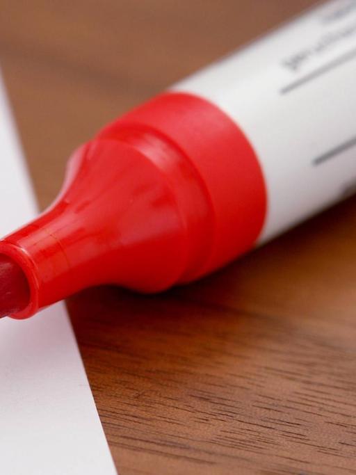 Ein roter Filzstift malt ein Ausrufezeichen auf ein Blatt Papier.
