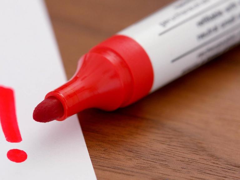 Ein roter Filzstift malt ein Ausrufezeichen auf ein Blatt Papier.