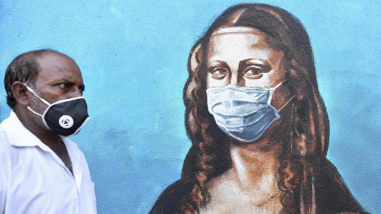 Ein Mann mit Mundschutz geht an einem Wandgemälde vorbei, auf dem auch die Mona Lisa Mundschutz trägt. Ein Mann mit Mundschutz geht an einem Wandgemälde vorbei, auf dem auch die Mona Lisa Mundschutz trägt.