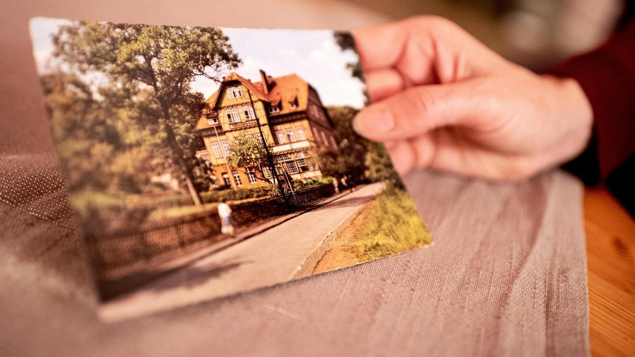 Eine Hand hält eine Postkarte mit der Ansicht der Kinderheilanstalt Waldhaus in Bad Salzdetfurth.