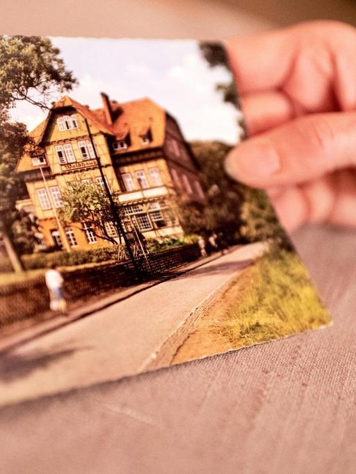 Eine Hand hält eine Postkarte mit der Ansicht der Kinderheilanstalt Waldhaus in Bad Salzdetfurth.